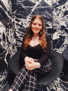A young women sitting in a chair in front of a black and white background