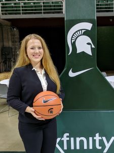 Woman with long, blond hair holding a basketball next to a Spartan Helmet banner