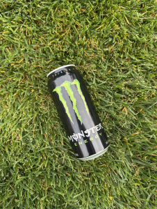 A monster energy drink can rests on the grass