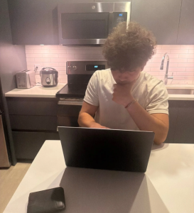 A person concentrates on a laptop screen while sitting in a kitchen