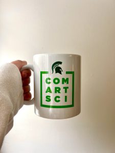 A coffee mug that says Com Art Sci