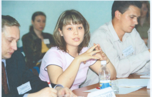 A woman speaks while sitting at a table of a conference.