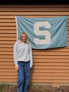 A woman stands in front of a "Spartan Block S" flag.