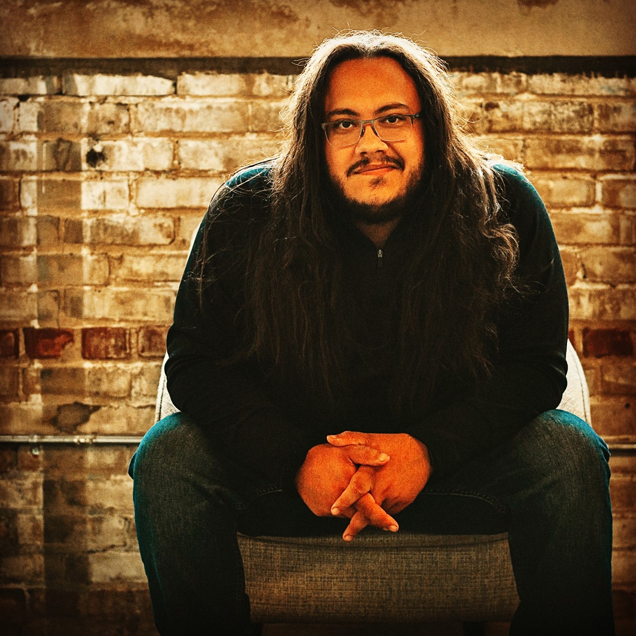 Male with long brown hair sitting in a chair