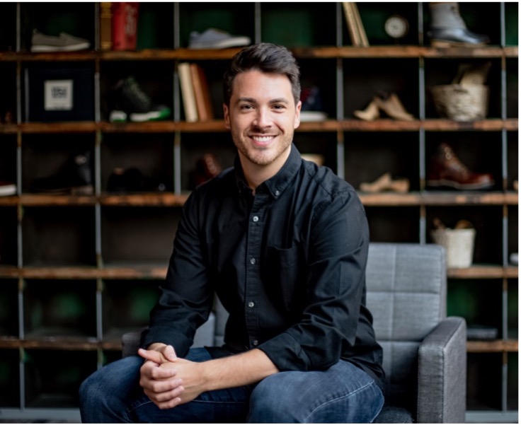 Portrait of smiling man in relaxed office with shoes on shelves. The man is sitting in a chair.