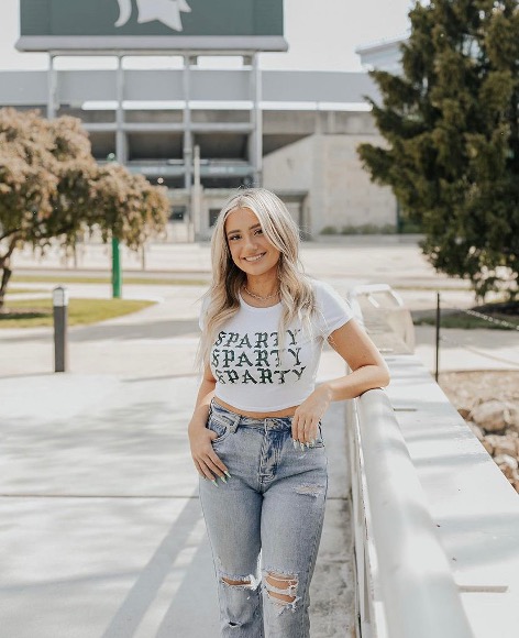 Woman wearing MSU clothing, standing in front of MSU stadium