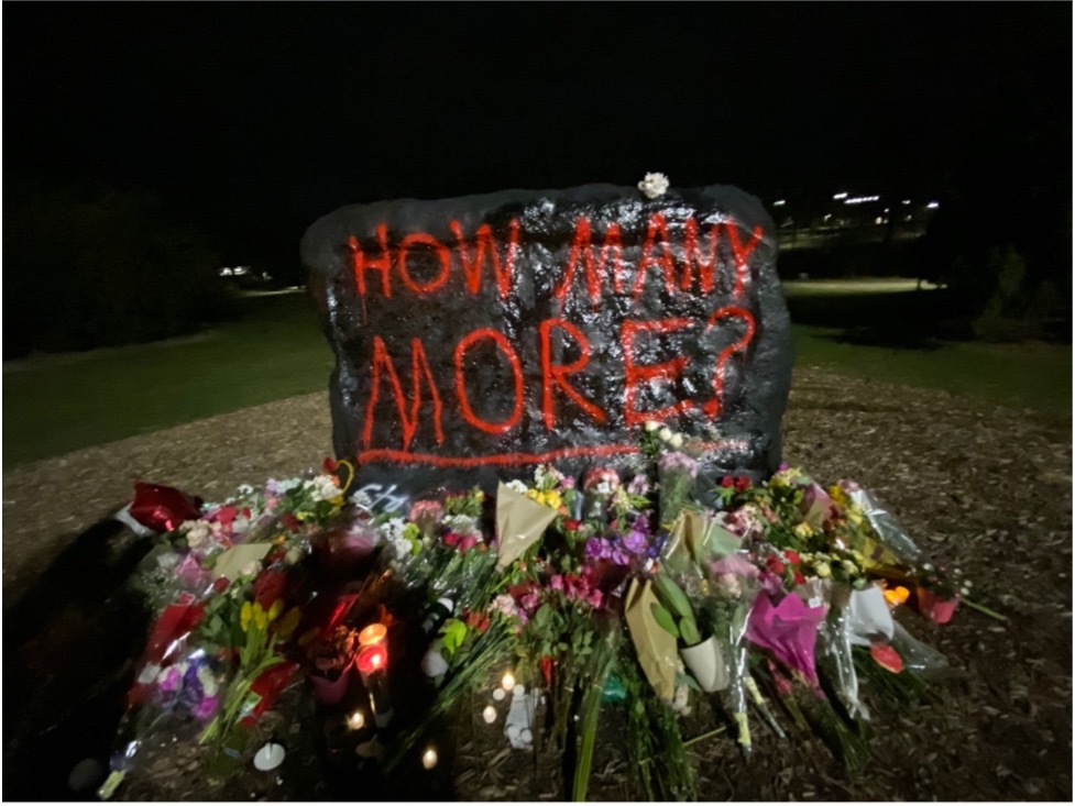 Photograph of MSU's "rock" where students decorate with various thoughts and expressions; the rock is black with red text, "How Many More?"