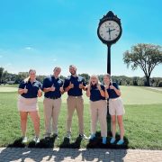 An exterior photograph of five students smiling near a large clock.