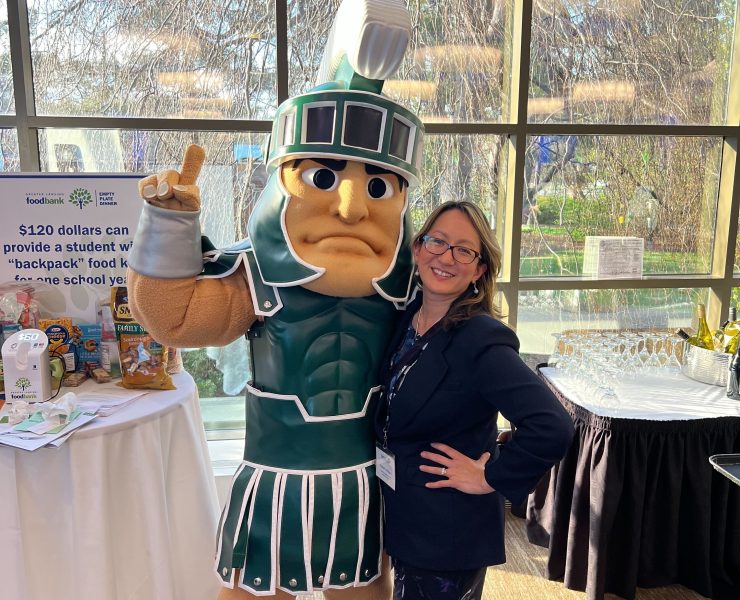 A person smiles while posing with Michigan State University mascot, Sparty.