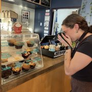 A person takes pictures of baked goods in a coffee shop.