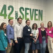 Students posing in front of a large sign for 42pointSEVEN.