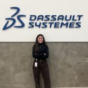 A person smiles while posing in front of a wall with a large business logo.