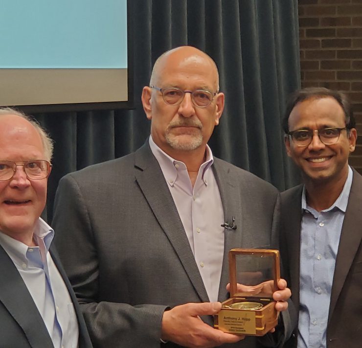 Three people pose while smiling. One person holds an award.