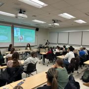 Students sit in chairs listening to presenters who are also sitting in chairs