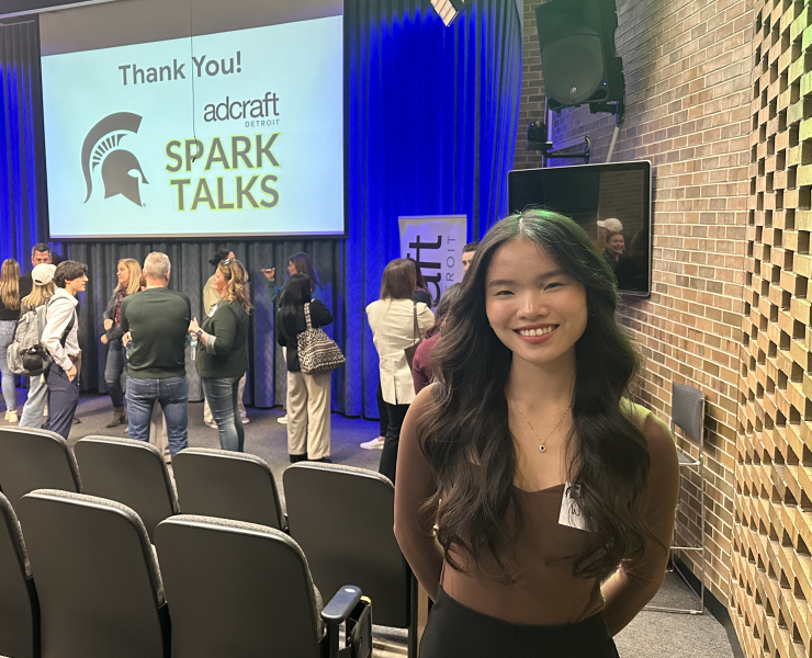 An MSU student stops for a photograph in front of an event stage for AdCraft Detroit, Spark Talks