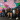 Six people smile while sitting for a photo in front of a multi-colored mural.