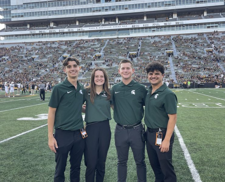 Four MSU students pose in front of large crowd at Kinnick Stadium