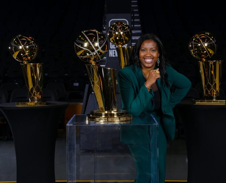 A person smiles posing near a basketball trophy