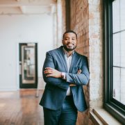 A smiling person posing next to a window