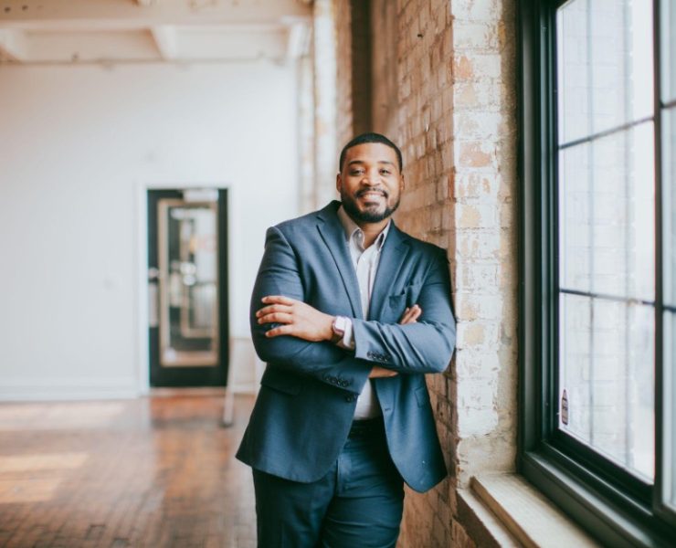 A smiling person posing next to a window