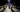 A group of people solemnly look at an art exhibit in a dimly lit room