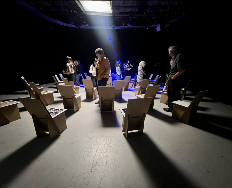 A group of people solemnly look at an art exhibit in a dimly lit room