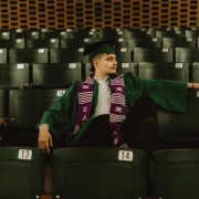 A person sitting in graduation attire in a seats in a classroom