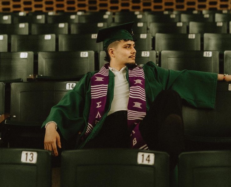 A person sitting in graduation attire in a seats in a classroom