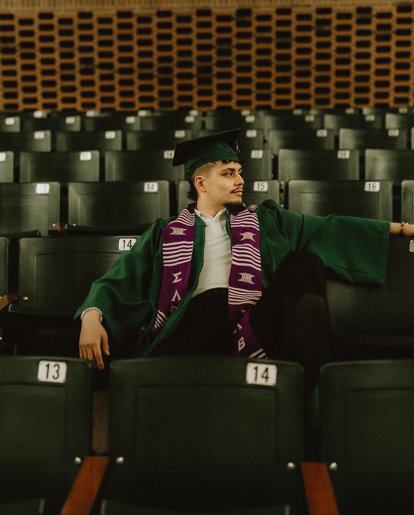 A person sitting in graduation attire in a seats in a classroom