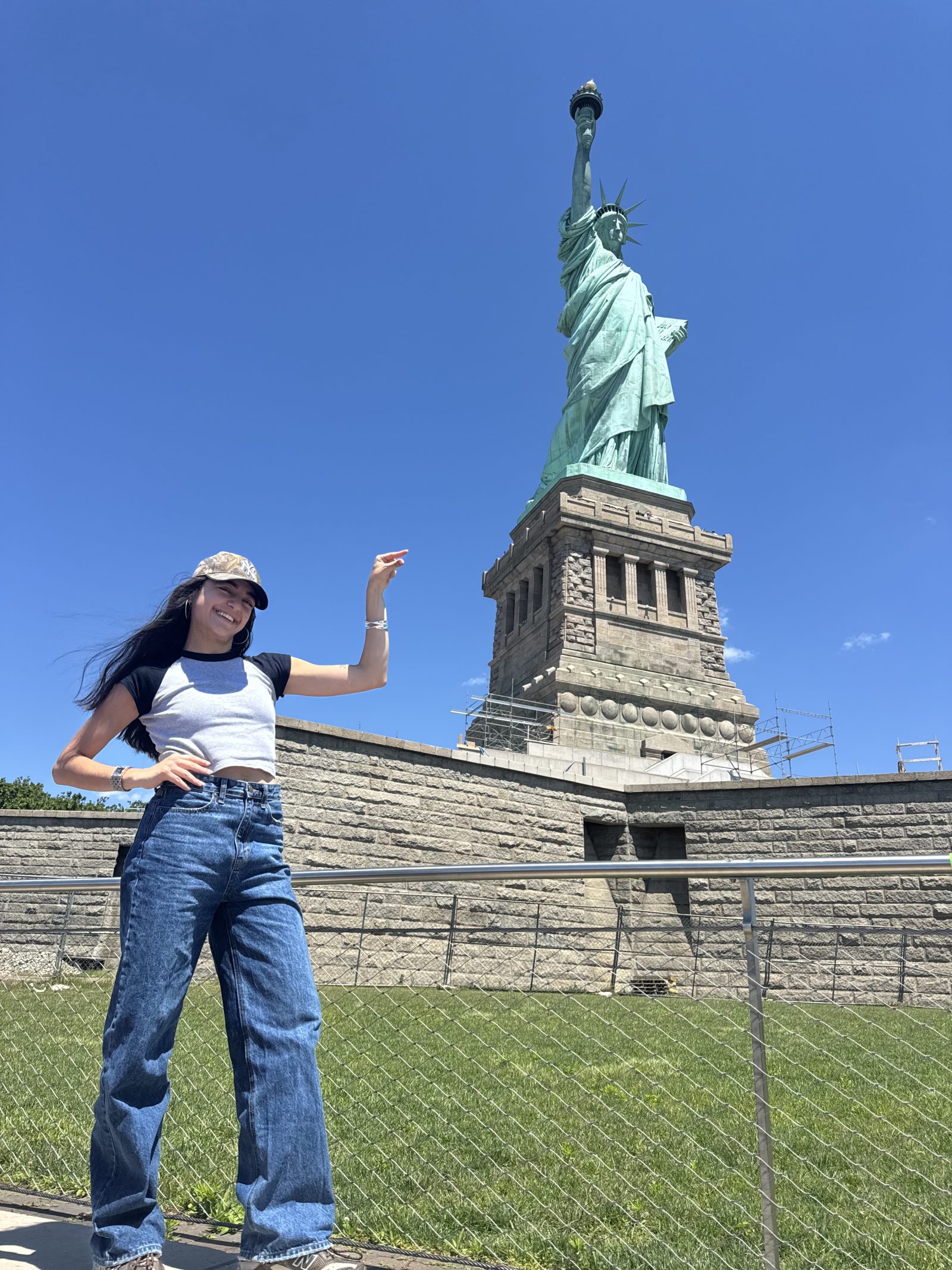 A person poses in front of the Statue of Liberty