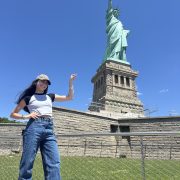 A person poses in front of the Statue of Liberty