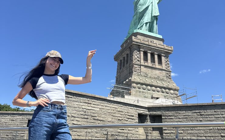A person poses in front of the Statue of Liberty