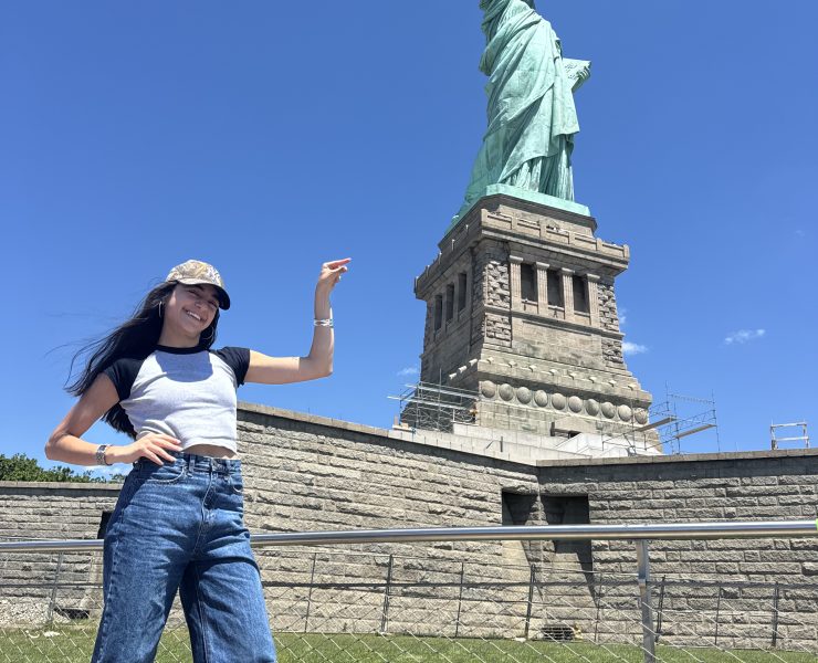 A person poses in front of the Statue of Liberty