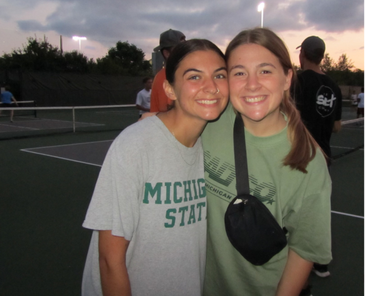 Two students smile while posing for a photograph outside