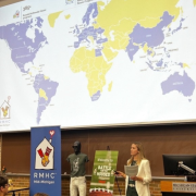 a woman presents with a map of the world behind her