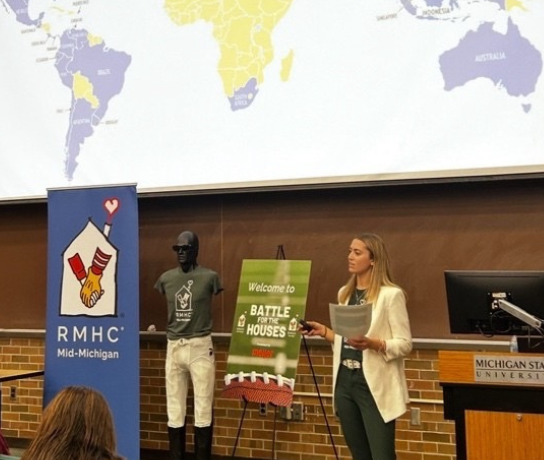 a woman presents with a map of the world behind her