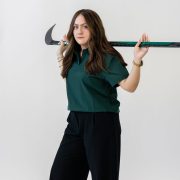 A person poses on a white background with a hockey stick