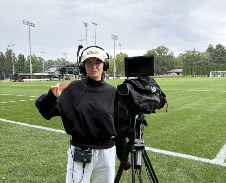 A woman gives a thumbs up next to a broadcast camera on a football field