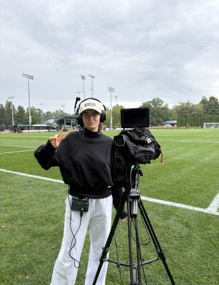 A woman gives a thumbs up next to a broadcast camera on a football field