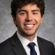 A person smiles in front of a gray background