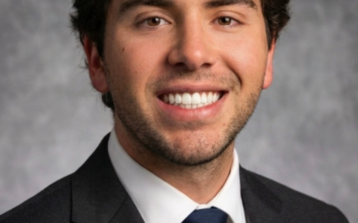 A person smiles in front of a gray background