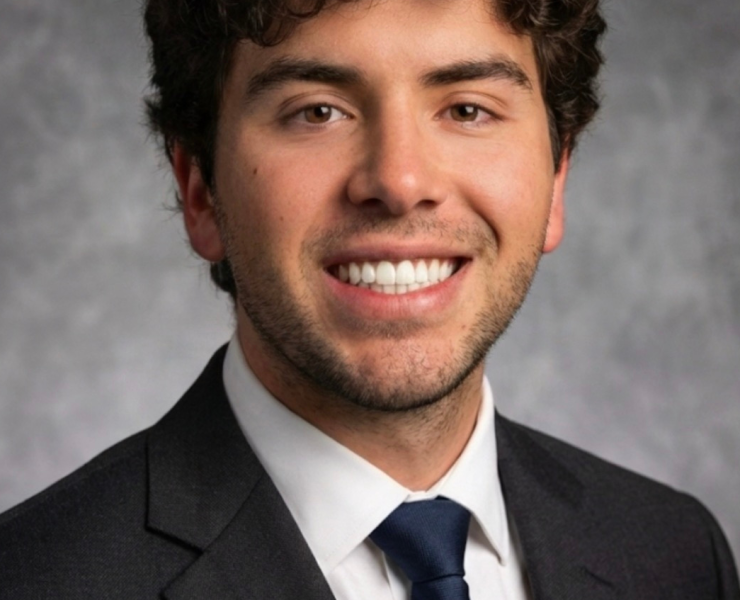 A person smiles in front of a gray background