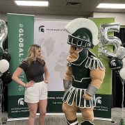 A woman poses looking at college mascot Sparty.