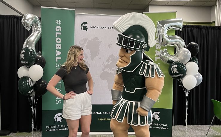 A woman poses looking at college mascot Sparty.