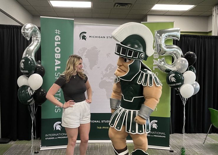 A woman poses looking at college mascot Sparty.