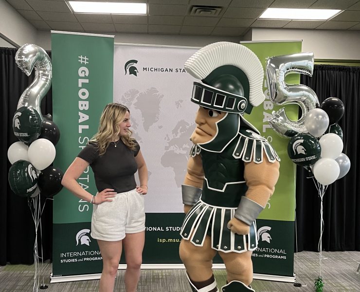 A woman poses looking at college mascot Sparty.
