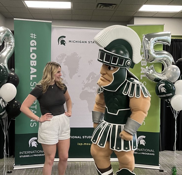 A woman poses looking at college mascot Sparty.