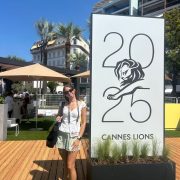 A person poses in front of a large adertisement for Cannes Lions 2025