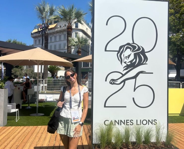 A person poses in front of a large adertisement for Cannes Lions 2025