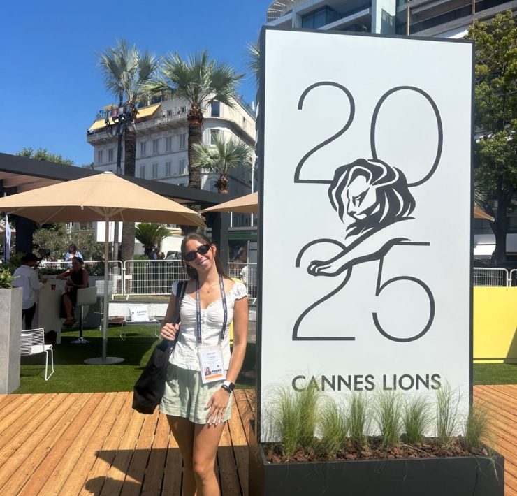 A person poses in front of a large adertisement for Cannes Lions 2025